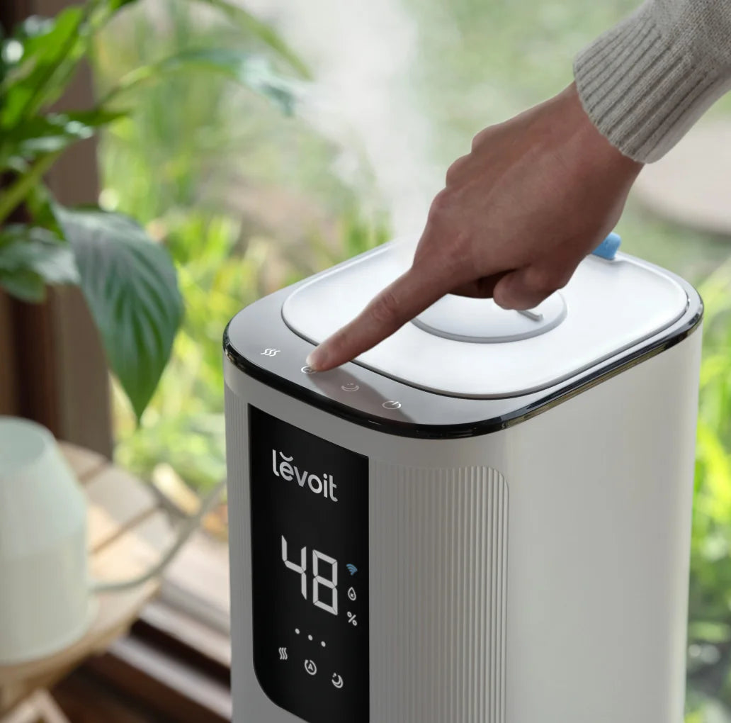 Hand adjusting settings on Levoit OasisMist 1000S ultrasonic humidifier, best humidifier for large room with digital display.