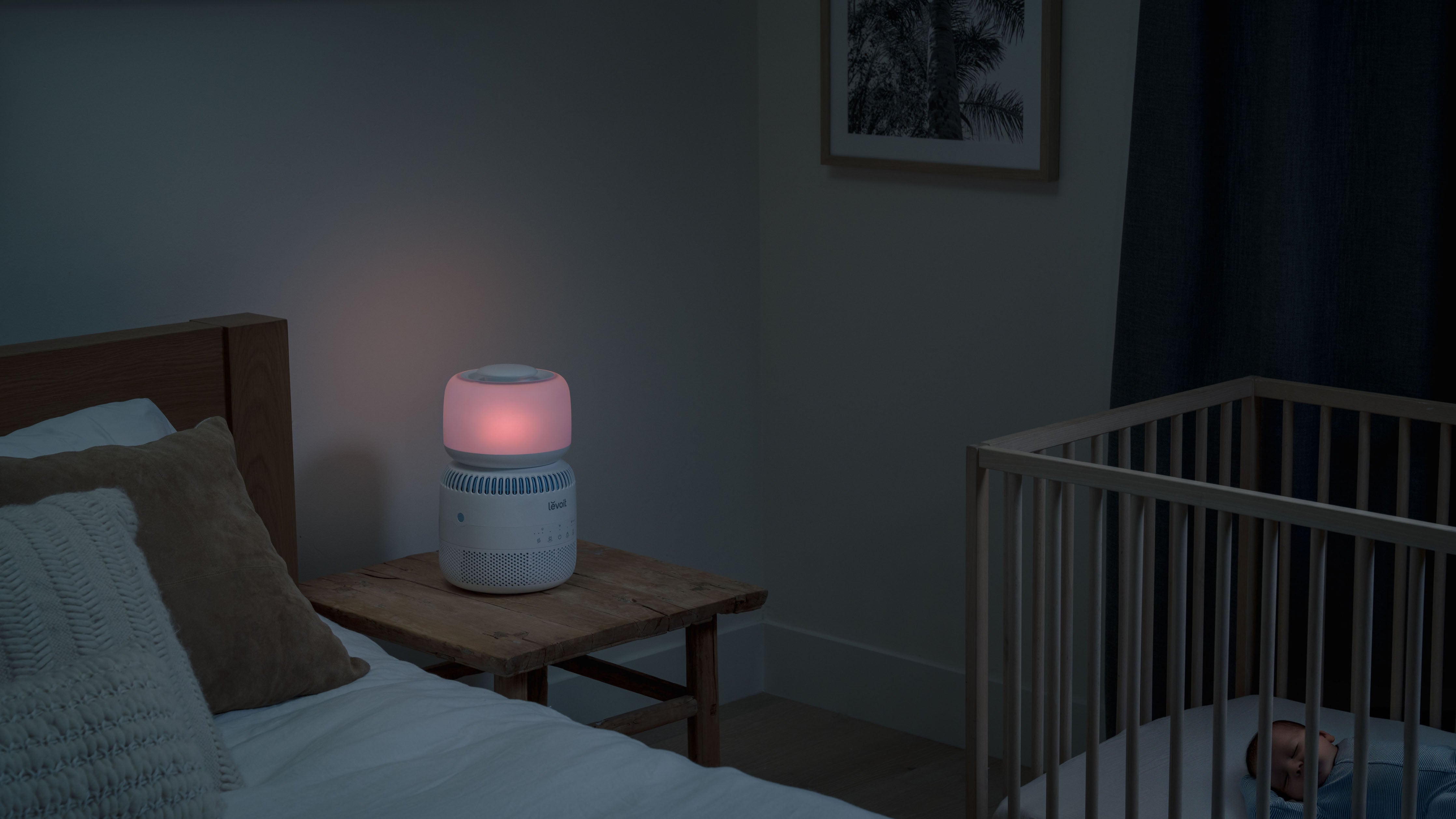 Baby asleep in crib next to bed and nightstand with Sprout Humidifier, which has nightlight lit