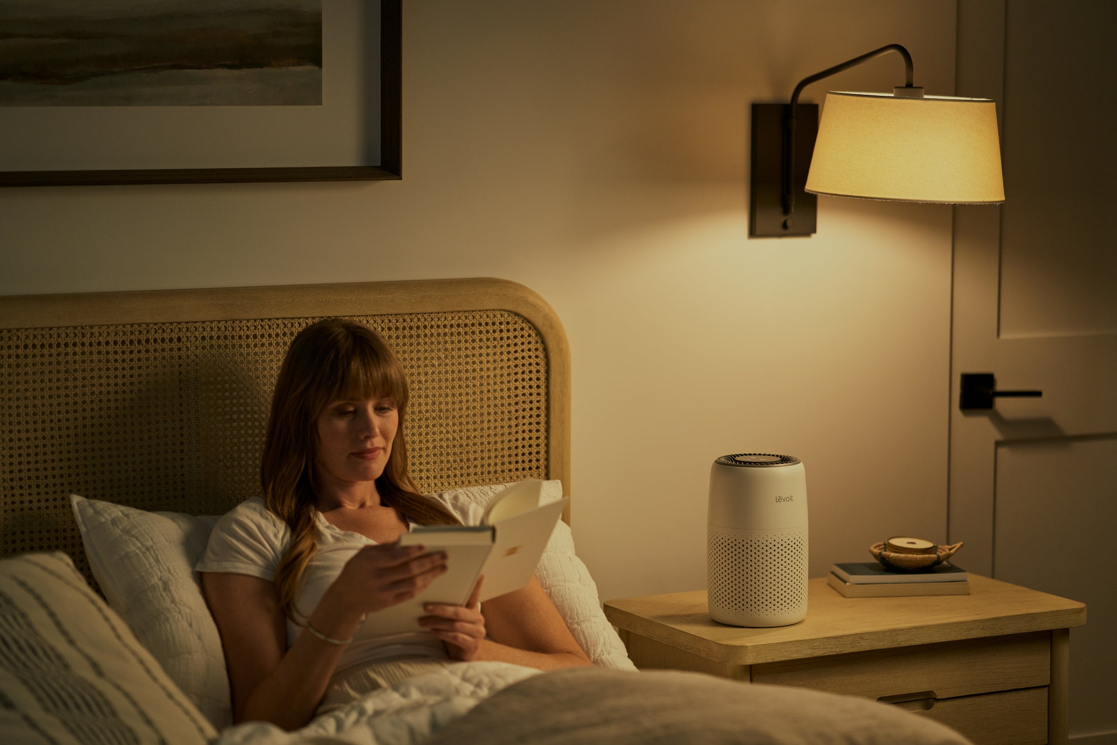 Woman reading in bed next to Levoit air purifier
