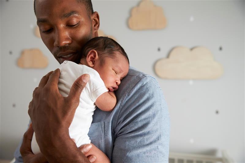 Man holding newborn baby asleep on his shoulder