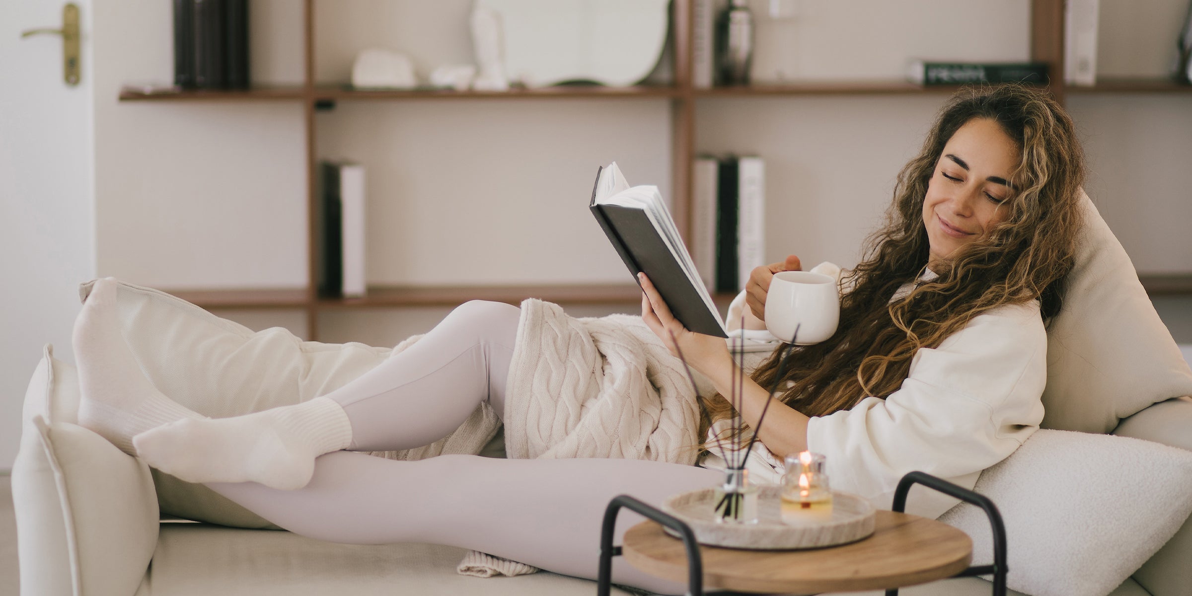 Woman reading book on couch with cup of tea