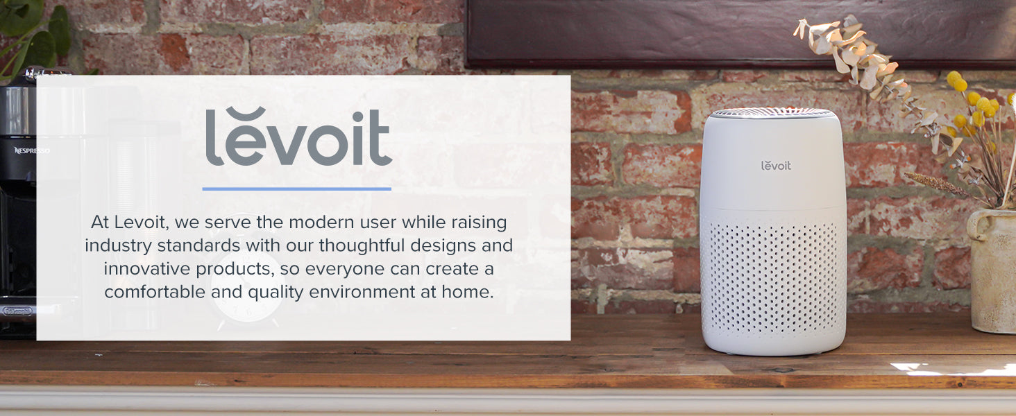 A white air purifier sits on a wooden table against a brick wall, with decorative plants nearby. Text promotes Levoit products.